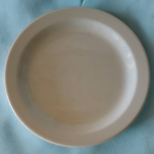 Pode incluir: Um prato de cerâmica branco simples com uma borda ligeiramente elevada.