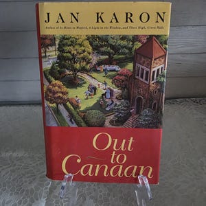 May include: A hardcover book titled "Out to Canaan" by Jan Karon. The book has a red and yellow cover with the title in gold lettering. The cover art depicts a church and a park scene with people. The author's name is at the top.
