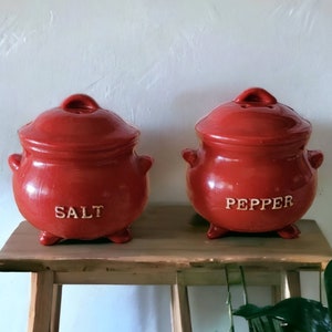 May include: Two red ceramic salt and pepper shakers with white lettering. The salt shaker says "SALT" and the pepper shaker says "PEPPER".