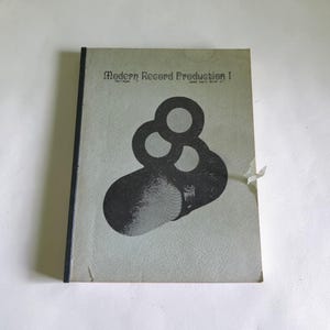 May include: A softcover book titled Modern Record Production I by James Vesty Smith Jr. The cover is light grey with a textured finish and features a large black graphic of overlapping circles and a capsule shape. The spine is black.