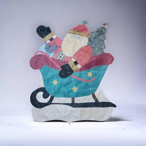 May include: A festive Christmas decoration featuring a Santa Claus figure in a blue and green sleigh with a small Christmas tree. The Santa Claus is wearing a red and white suit and has a white beard. The sleigh is decorated with stars and has a black and white striped pattern.