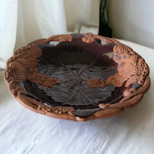 May include: A brown ceramic bowl with a dark brown glaze and a raised design of grapes and leaves around the rim.