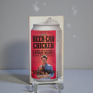May include: A cookbook titled "Beer-Can Chicken" with a red and white can design. The cover features the text "A Barbecue! Bible Cookbook" and "And 74 Other Offbeat Recipes For The Grill!" with an image of the author.