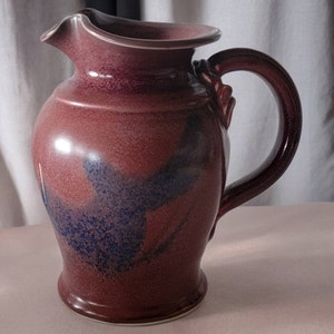 May include: A brown ceramic pitcher with a blue and white glaze design. The pitcher has a wide mouth and a handle.