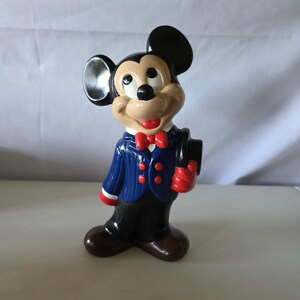 K&ouml;nnte beinhalten: Eine Keramikfigur von Mickey Mouse in einem blauen Anzug mit roten Akzenten, einer roten Fliege und einem schwarzen Zylinder. Die Figur hat braune Schuhe und eine schwarze Hose. Die Figur steht aufrecht.