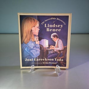 May include: A book cover titled "The Incredible Discovery of Lindsey Renee" by Joni Eareckson Tada, illustrated by Irena Roman. The cover shows illustrations of a young woman and an older person at a computer, set against a dark blue backdrop.