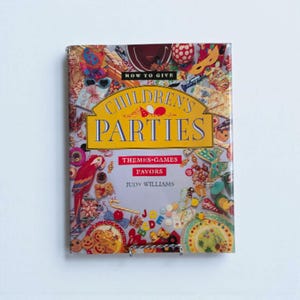 May include: A hardcover book titled "CHILDREN'S PARTIES" with the subtitle "THEMES GAMES FAVORS" by Judy Williams. The cover features a collage of party-related items in various colors, including a parrot, masks, and cookies.