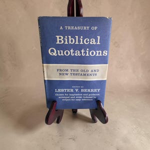 May include: A blue hardcover book titled A Treasury of Biblical Quotations from the Old and New Testaments, edited by Lester V. Berrey. The cover features white text on a blue background with a central horizontal light gray band and dark text.