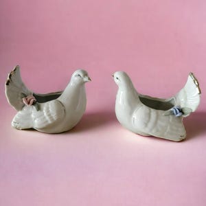 May include: Two white ceramic dove planters with floral accents. The doves are facing opposite directions and have a small opening for planting.