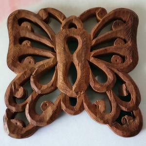 May include: A brown wooden butterfly wall decor with intricate carvings. The butterfly is carved in a delicate, ornate style, with a detailed design on its wings.