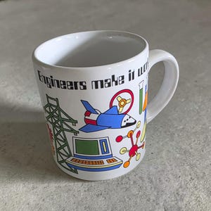 May include: A white ceramic mug featuring the black text Engineers make it work and a colorful graphic print including a blue space shuttle, a green electrical tower, a computer, a red and yellow steering wheel, and a red molecular structure.