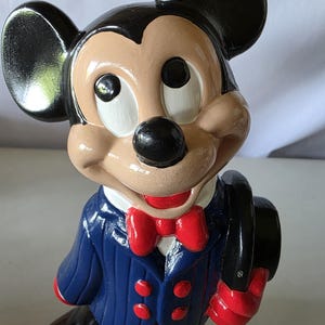 K&ouml;nnte beinhalten: Keramikfigur von Mickey Mouse, mit einem schwarzen Zylinder, einem blauen Anzug mit roten Kn&ouml;pfen und einer roten Fliege. Die Figur hat ein beiges Gesicht, schwarze Ohren und eine schwarze Nase. Die Figur h&auml;lt einen schwarzen Zylinder.