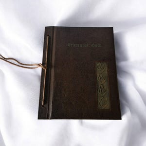 以下が含まれることがあります： 表紙に「Readers of Gold」というタイトルが刻印された、茶色の革装丁のジャーナル。ジャーナルの表紙の右側には装飾的なデザインが施されています。