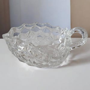 May include: A clear glass serving dish with a textured, diamond-shaped pattern and a handle. The dish is designed for serving small items like candy or nuts.