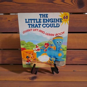 May include: A children's book titled "The Little Engine That Could" with a blue train illustration. The cover features the text "Giant Lift-and-Learn Book" and a yellow starburst with "More than 65 flaps!"