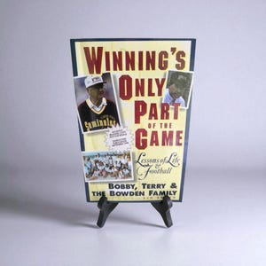 May include: A framed print with the text "WINNING'S ONLY PART OF THE GAME" in red and white. The print includes images of football coaches and a team photo. The print is displayed on a black easel.