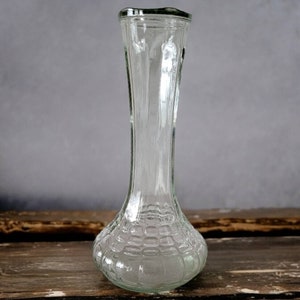 Op de afbeelding: Een heldere glazen vaas met een getextureerde, bolvormige basis en een lange, slanke hals.
