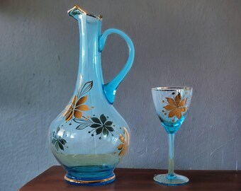 May include: A blue glass pitcher with a gold floral design and a matching blue glass wine glass with a gold floral design.