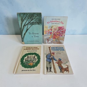 May include: Four hardcover children's books titled To Know a Tree, It's Valentine's Day, Stories from a Snowy Meadow, and Snowshoe Thompson. The covers feature illustrations of a tree, a Valentine's shop, mice in a wreath, and a person with skis.