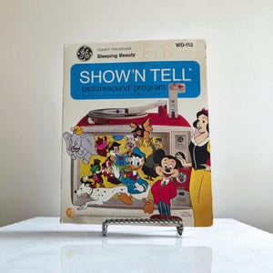 Puede incluir: Programa de imágenes y sonido Show'n Tell de GE vintage con personajes de Disney. La portada muestra una colorida ilustración de Mickey Mouse, el Pato Donald y Blancanieves. El texto de la portada dice "SHOW'N TELL picturesound program" y "Sleeping Beauty".