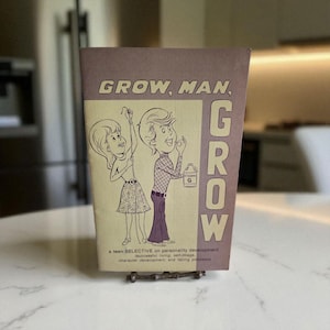 Peut inclure: Livre vintage intitulé « GROW, MAN, GROW » avec des illustrations de dessins animés d'un garçon et d'une fille. La couverture est violet clair avec le titre en grandes lettres en gras. Le sous-titre du livre se lit « a teen SELECTIVE on personality development ».