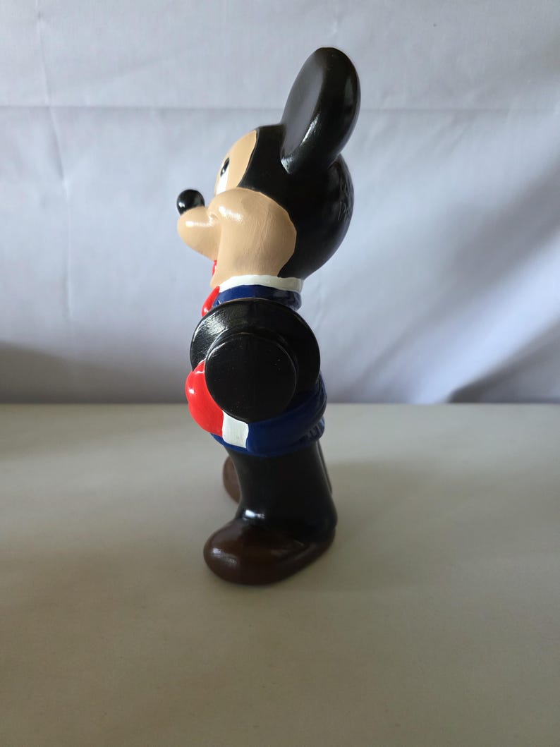 K&ouml;nnte beinhalten: Vintage Mickey Mouse Figur, bemalt in Schwarz, Beige, Rot, Blau und Braun. Die Figur tr&auml;gt eine blaue Jacke mit roten und wei&szlig;en Akzenten, einen schwarzen Hut und braune Schuhe. Ein Sammlerst&uuml;ck.