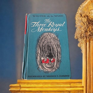May include: A vintage book titled "The Three Royal Monkeys" by Walter de la Mare. The book has a teal cover with an illustration of a forest scene and three figures in red. The book is illustrated by Mildred E. Eldridge.