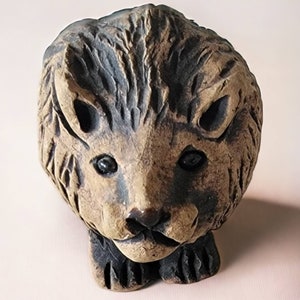 May include: A detailed, hand-carved lion head sculpture. The sculpture is primarily brown with darker accents, showcasing a textured mane and facial features. The lion's eyes are dark, and the overall design is rustic and artistic.