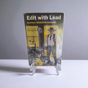 May include: Vintage book cover titled "Edit with Lead" by George Madison Grooms. The cover art depicts a cowboy in a hat and vest standing in front of a saloon. The background is a sepia tone with a wanted poster.