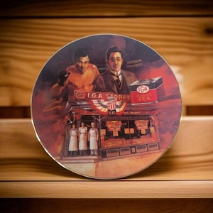 May include: A round ceramic plate with a colorful image of a boxing scene, a man in a suit, and a grocery store. The plate features the text "IGA Stores" and "Empress Thornton".