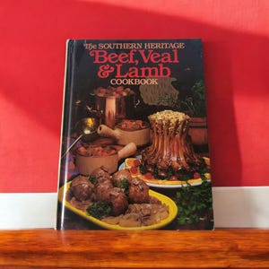 May include: A vintage cookbook titled "The Southern Heritage Beef, Veal & Lamb Cookbook". The cover features a variety of cooked meats, including a roast, meatballs, and a casserole.