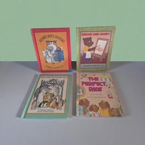 Puede incluir: Se muestran cuatro libros infantiles, cada uno con ilustraciones coloridas. Los títulos incluyen "Henry's Awful Mistake", "Bread and Honey", "Where Will the Animals Stay?" y "The Perfect Ride". Los libros están sobre una superficie gris claro.