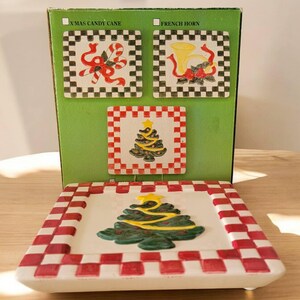 Puede incluir: Conjunto de cuatro posavasos de cerámica con temática navideña con diseños de cuadros rojos y blancos. Los posavasos presentan un árbol de Navidad, un bastón de caramelo, un cuerno francés y un árbol de Navidad.
