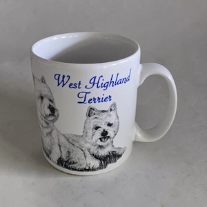 Op de afbeelding: Een witte keramische mok met een zwart-witte illustratie van twee West Highland Terriërs. De tekst West Highland Terrier staat in een blauw cursief lettertype boven de honden gedrukt. De mok is voorzien van een standaard handvat.