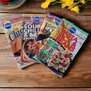 Op de afbeelding: Vier Pillsbury kookboeken met kleurrijke omslagen met afbeeldingen van voedsel. De kookboeken zijn getiteld "Nieuwe soep, chili en broodrecepten", "Geweldige caloriearme recepten", "Pasta, rijst en bonen" en "Amerikaanse klassiekers".