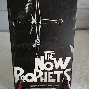 Peut inclure: Une couverture de livre en noir et blanc intitulée The Now Prophets Program Resource Book 1969. La couverture présente une illustration graphique à fort contraste d'une personne tenant un objet en forme de croix, avec du texte blanc.