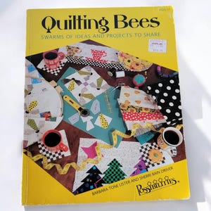 May include: A yellow book titled "Quilting Bees" with the subtitle "Swarms of Ideas and Projects to Share." The cover features quilting supplies, fabric swatches, and coffee cups. The book is by Barbara Tone Lister and Sherri Bain Driver.