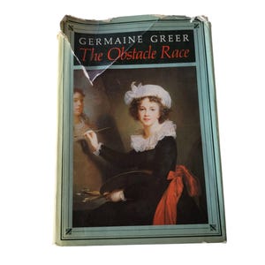 May include: A vintage hardcover book titled "The Obstacle Race" by Germaine Greer. The cover features a portrait of a woman in a black dress, white collar, and a red bow. The book has a light blue border and is slightly damaged.