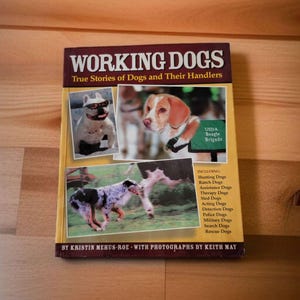 May include: A book titled "Working Dogs: True Stories of Dogs and Their Handlers" with a yellow cover and photos of dogs. The book includes stories about hunting dogs, ranch dogs, assistance dogs, therapy dogs, sled dogs, acting dogs, detection dogs, police dogs, military dogs, search dogs, and rescue dogs.