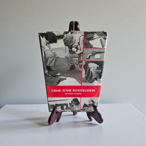 May include: A hardcover book titled Crime Scene Investigation by Kenneth W. Goddard. The cover features a collage of black and white photographs depicting forensic investigators at work, with a prominent red horizontal band across the center.