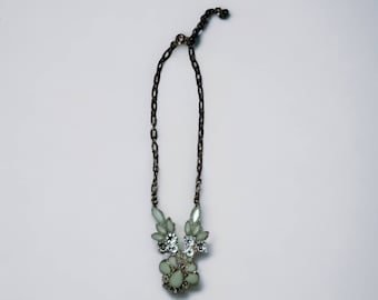 Pode incluir: Um colar de corrente prateada com um grande pingente adornado com strass branco e transparente.