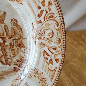 May include: A white ceramic plate with a brown floral design and a brown border. The plate has a letter "N" in the center and the number "9" on the bottom.