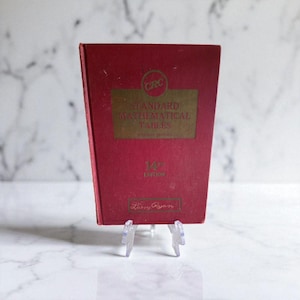 May include: A red book titled "Standard Mathematical Tables" with gold lettering. The book is the 14th edition and is displayed on a clear plastic stand. The book's cover has the author's name, Larry Ryan, printed on it.