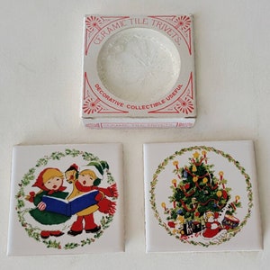 Può includere: Due sottopentola in ceramica a tema natalizio, uno con un albero di Natale e l'altro con due bambini che cantano canti natalizi. I sottopentola sono in una scatola che dice "Ceramic Tile Trivets Decorative Collectible Useful".