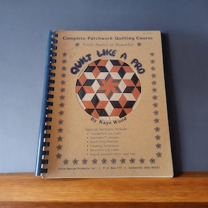May include: A brown book with a spiral binding titled "Quilt Like a Pro: Complete Patchwork Quilting Course From Basics to Beautiful" by Kaye Wood. The cover features a colorful geometric quilt design.