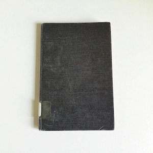 May include: A rectangular, black book with a textured cover. A small, rectangular sticker is affixed to the lower left corner. The book is set against a white background.