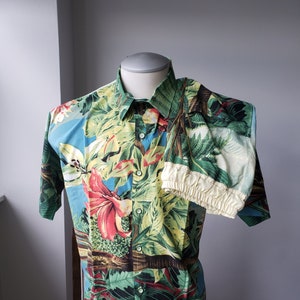 May include: A tropical print short-sleeved button-up shirt and matching shorts set. The shirt and shorts feature a vibrant green, red, yellow, and blue floral pattern.