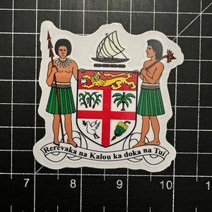 May include: A sticker featuring the Fiji coat of arms. Two figures flank a shield with a lion, palm trees, and a dove. The shield is topped with a boat and the text "Rerevaka na Kalou ka doka na Tui" is at the bottom.