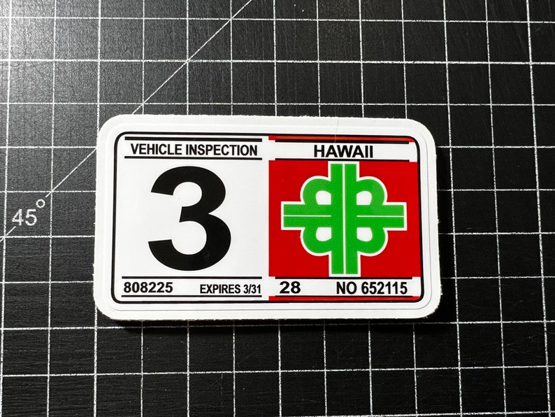 May include: White sticker with black text "VEHICLE INSPECTION" and a large black number "3". Below the number is "808225 EXPIRES 3/31". On the right side of the sticker is a red rectangle with white text "HAWAII" and a green four-leaf clover symbol. Below the symbol is "28 NO 652115".