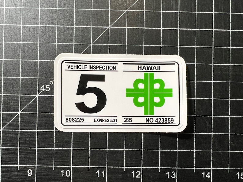 May include: White sticker with black text that reads "VEHICLE INSPECTION" and "HAWAII". The sticker has a large black number "5" and a green symbol of a four-leaf clover. The sticker also has the text "808225", "EXPIRES 5/31", "28", and "NO 423859".